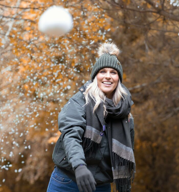 Woman smiling while throwing a snowball in a winter forest scene, capturing unexpected moments related to funerals.