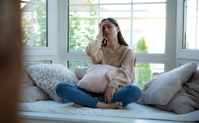 Stressed woman sitting on sofa holding pillow upset after realizing immature guy has treated many girls the same way before.