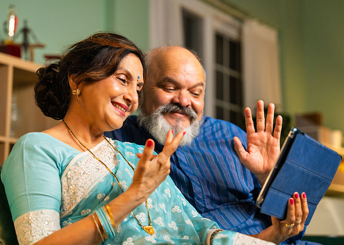 Middle-aged parents using a tablet, smiling and waving during a video call, depicting a family held hostage scenario.