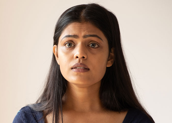 Worried young woman with long dark hair, looking anxious and uncertain about being held hostage at parents&rsquo; place.