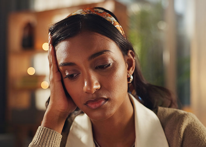 Young woman looking distressed and worried, sitting indoors, depicting the feeling of being held hostage at parents&rsquo; place.