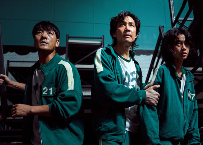 Three people in green tracksuits with numbers, portraying characters related to Squid Game prank investigation.