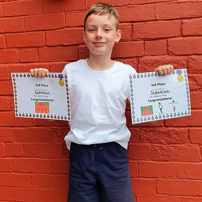 Schoolboy holding certificates against red brick wall, related to investigation of squid game prank incident.
