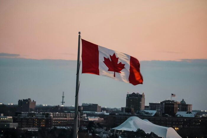 Canadian flag waving over a cityscape at dusk as people share historical facts unknown until recently.
