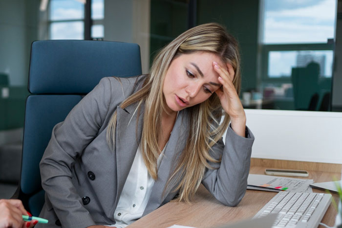 Woman looking conflicted at her desk in an office setting after a coworker told her to stay home and birth babies. Woman looking conflicted at her desk in an office setting after a coworker told her to stay home and birth babies.