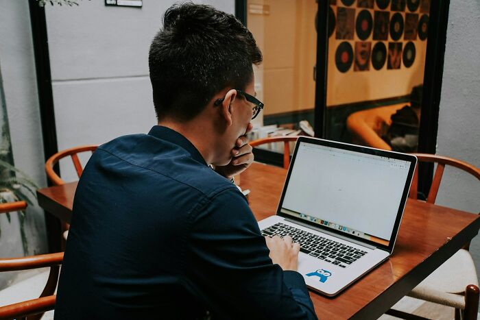 Man in glasses sitting at wooden table using laptop, reflecting on moments that made chefs stop cooking professionally.