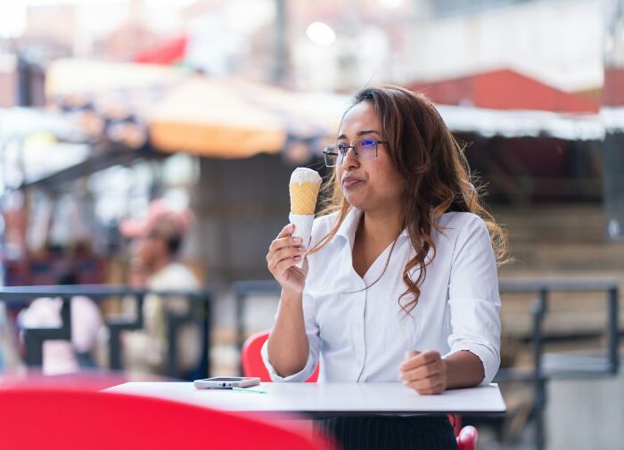Woman in glasses eating ice cream cone outdoors, capturing a moment of true stories that sound made up but happened.