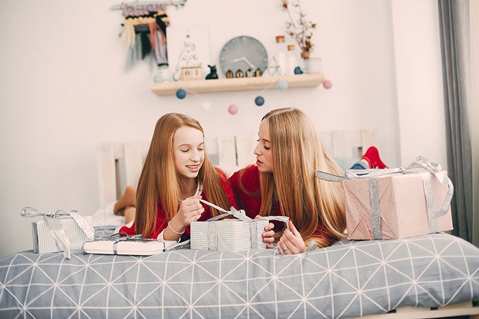 Mother and daughter opening Christmas presents on bed, with concern over promised $400 contribution per kid changing.