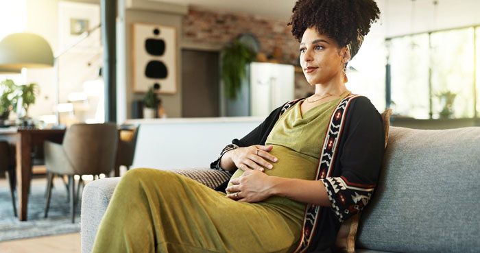Pregnant woman sitting on couch at home, reflecting on complicated feelings about adoption and race issues.