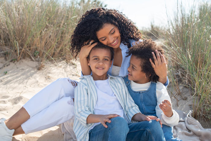 Woman with two mixed race children sitting outdoors on sand, reflecting on friend wanting white baby adoption conflict.