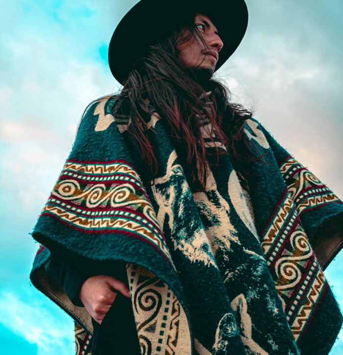 Person wearing a patterned poncho and wide-brimmed hat resembling a barefoot spiritual advisor at an outdoor setting.