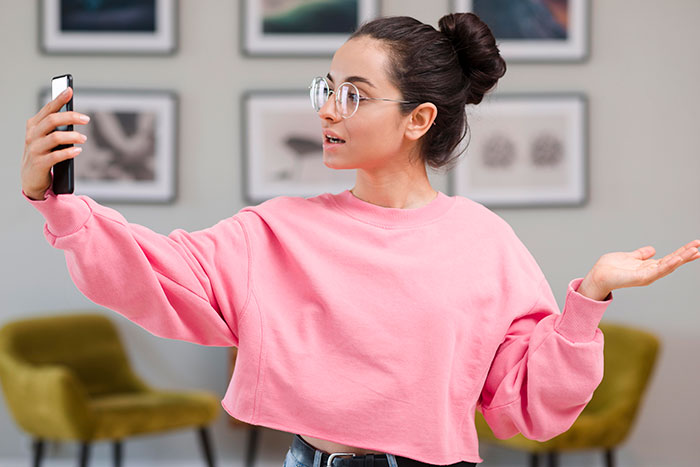Woman in pink sweatshirt taking a selfie, upset about sister building TikTok fame by lying about her.