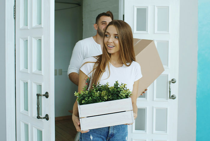 Young woman helping her brother and his wife by carrying a box of plants into their home showing family support and care. Young woman helping her brother and his wife by carrying a box of plants into their home showing family support and care.