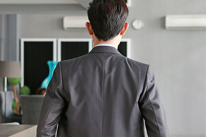 Man in gray suit from behind, symbolizing a clever criminal outsmarting police officers in a modern indoor setting.