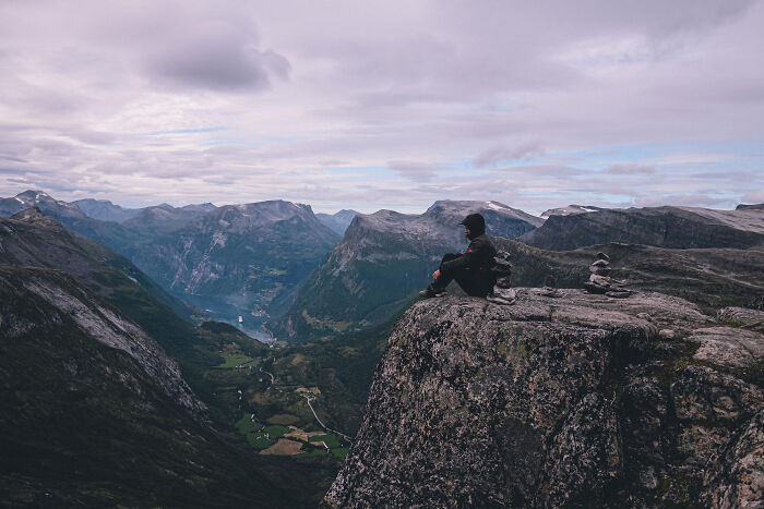 Person sitting on a mountain cliff overlooking a valley, symbolizing stories of those most likely to succeed with plot twists.