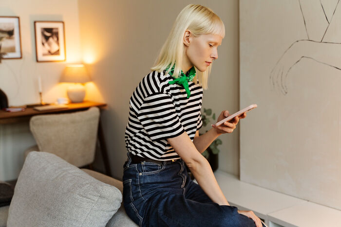 Young woman in striped shirt reading phone, reflecting on unexpected twists in stories about most likely to succeed.