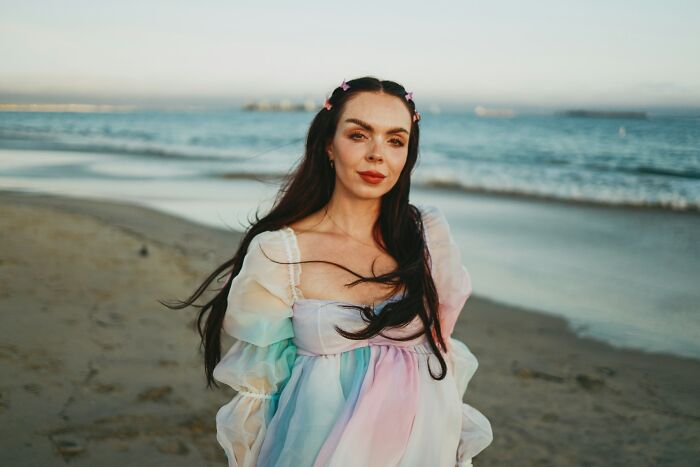 Young woman with long dark hair in a pastel dress standing on a beach, symbolizing most likely to succeed with plot twists.