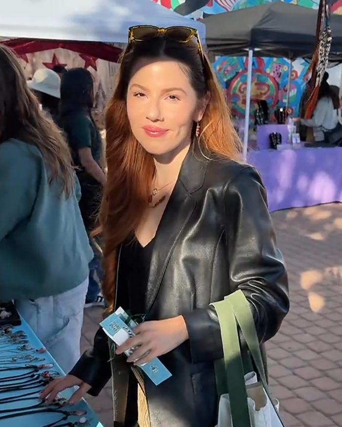 Young woman at outdoor market smiling, wearing black leather jacket and sunglasses, related to woke social media user topic. Young woman at outdoor market smiling, wearing black leather jacket and sunglasses, related to woke social media user topic.