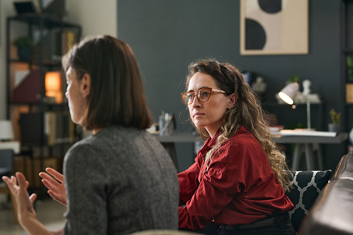 Two women engaged in conversation in a cozy room, illustrating psychological cheat codes for easier social life.