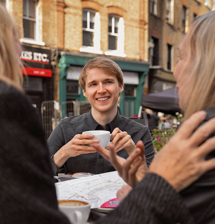 Young man smiling and holding a cup, engaging in social life using psychological cheat codes outdoors.