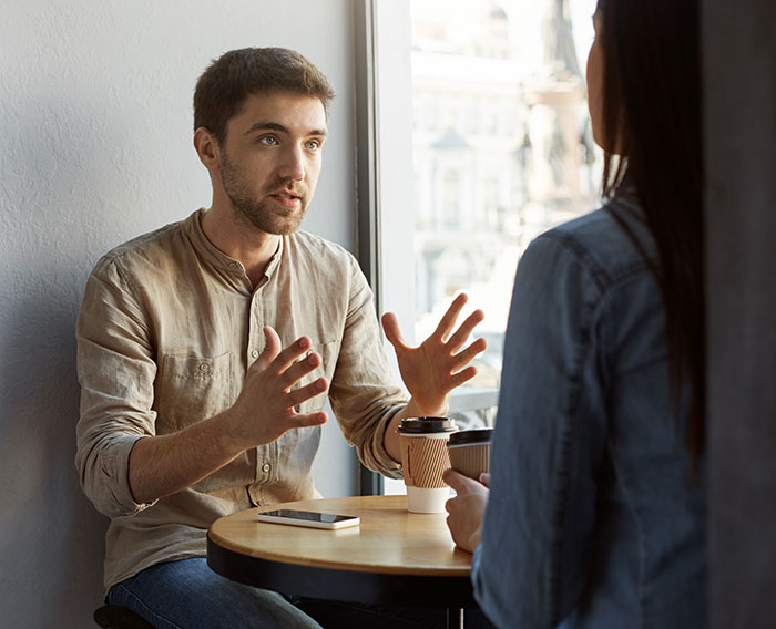 Two people having a conversation over coffee using psychological cheat codes for easier social life at a cafe table.