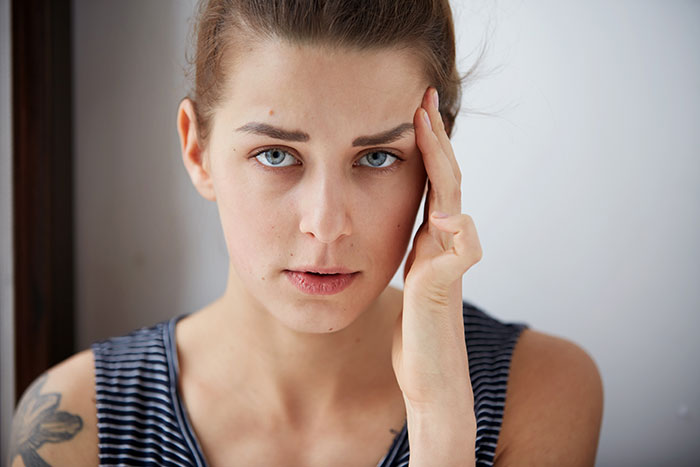 Young woman with a thoughtful expression touching her temple, illustrating psychological cheat codes for easier social life.