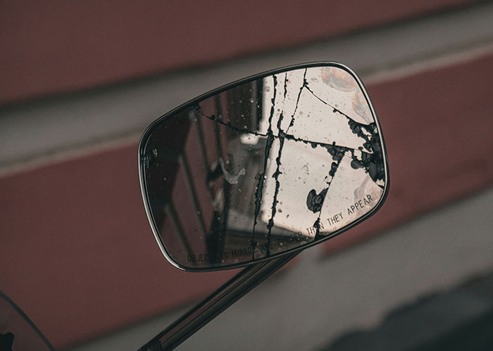 C*****d motorcycle mirror reflecting a blurred background, symbolizing diabolical revenge and unpredictable enemy actions.