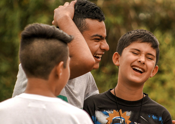 Three boys laughing together outdoors, capturing moments of friendship and diabolical revenge stories vibe.