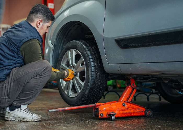 Man changing car tire using a jack in a garage, illustrating diabolical revenge stories and unexpected acts of retaliation.