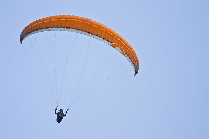 Person flying with an orange paraglider against a clear sky, capturing the panic on his face in mid-air.
