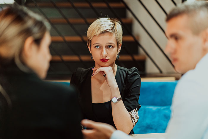 Woman with panic on her face sitting between two people during a serious conversation in a modern indoor setting.
