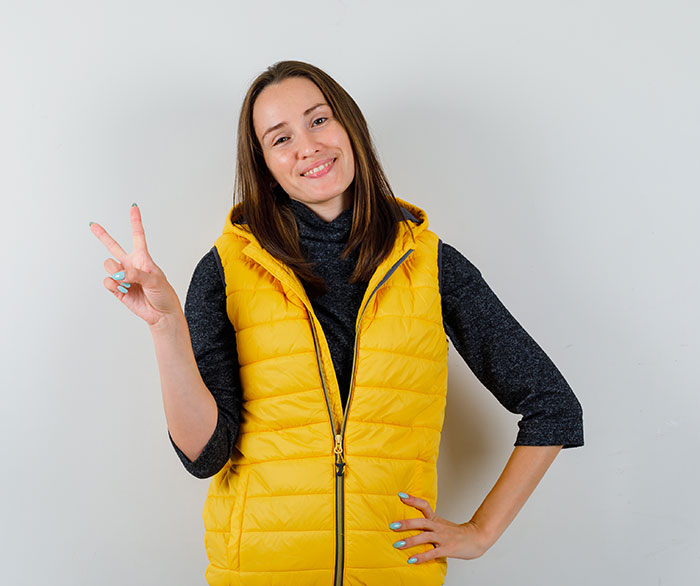Young woman in a yellow vest smiling and making a peace sign, contrasting the panic on his face theme.