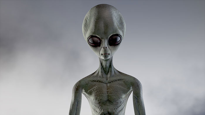 Grey alien figure with large black eyes showing panic on his face against a blurred neutral background