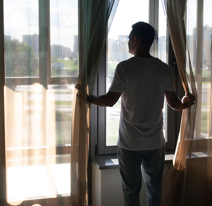 Man standing by a window looking outside with a serious expression showing the panic on his face.