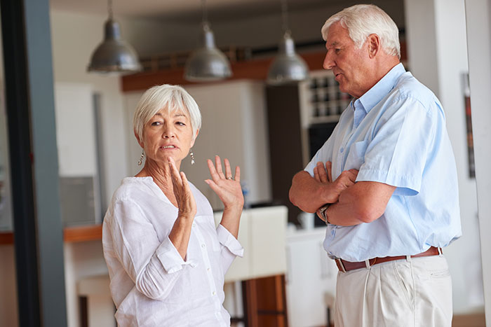 Older man and woman in kitchen, woman gesturing upset while man crosses arms, illustrating homemade pies conflict.