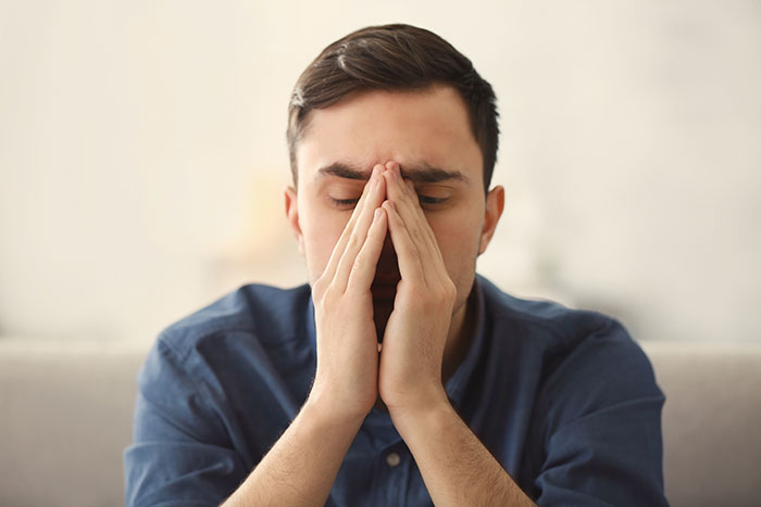 Man in a blue shirt with eyes closed and hands covering his face showing emotions people only started to believe in after experience