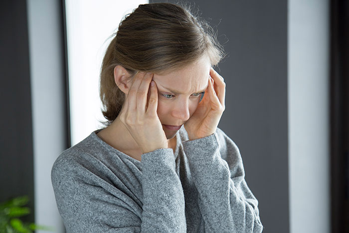 Woman in gray sweater holding temples, appearing stressed and deep in thought, reflecting on things people only believe once experienced.