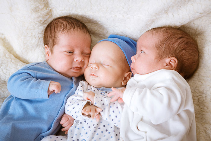Three newborn babies lying closely together on a soft blanket, illustrating experiences people only believe once it happens.