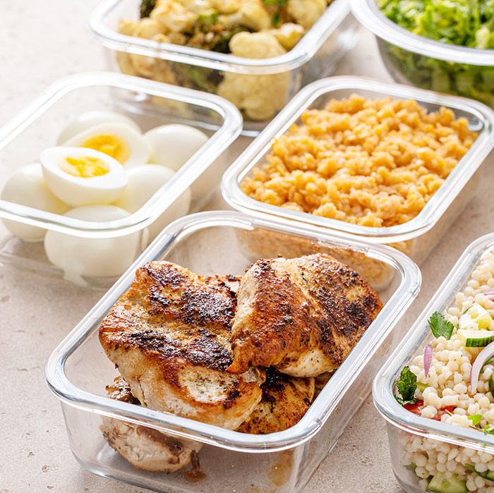 Glass containers with Thanksgiving leftovers including grilled chicken, boiled eggs, and side dishes on a kitchen counter