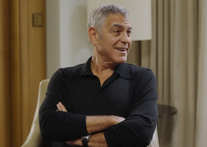 Man in a black shirt sitting with arms crossed, sharing vibes of celebrities people have met in casual setting.