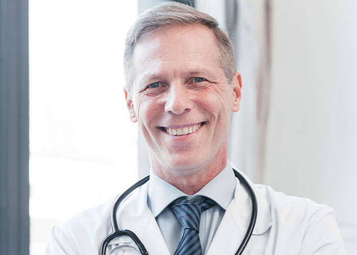 Smiling doctor with stethoscope in bright medical office, representing wild and funny post-anesthesia acts healthcare professionals encounter.