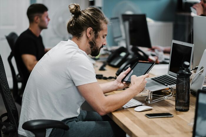 Man with a beard using a tablet and laptop at a desk, symbolizing stress before canceling wedding two months ahead.