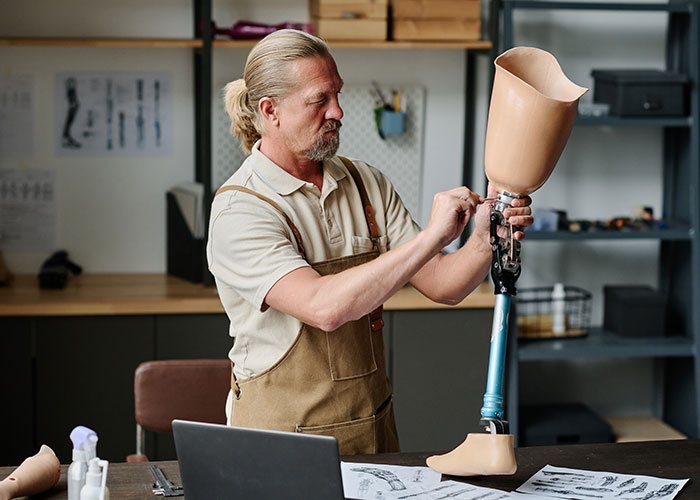 Man examining a prosthetic leg in a workshop, illustrating a man demands cousin pay for his cruel prank scenario.