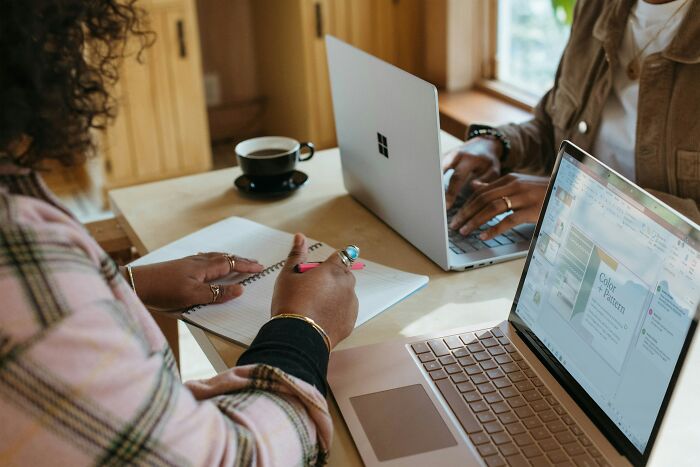 Two people working on laptops at a wooden table, one writing notes, relating to feeling betrayed by best friend and wanting space.