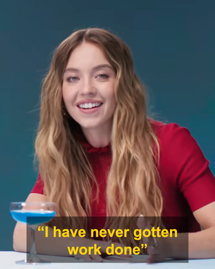 Sydney Sweeney speaking on rumors, denying plastic surgery in a red top against a blue background. Sydney Sweeney speaking on rumors, denying plastic surgery in a red top against a blue background.