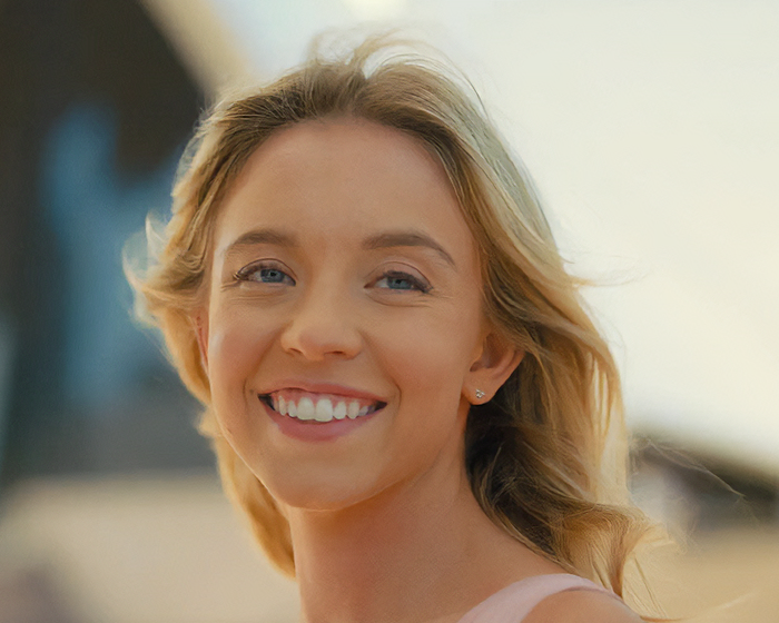 Sydney Sweeney smiling outdoors, showcasing natural beauty in soft lighting with a blurred background.