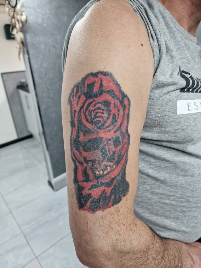 Close-up of a poorly done red and black tattoo on a person's upper arm, showcasing a design that might make members cringe.