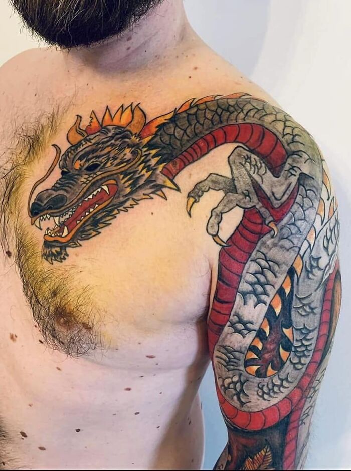 Colorful dragon tattoo covering a man’s shoulder and upper arm, showcasing detailed scales and fierce expression.