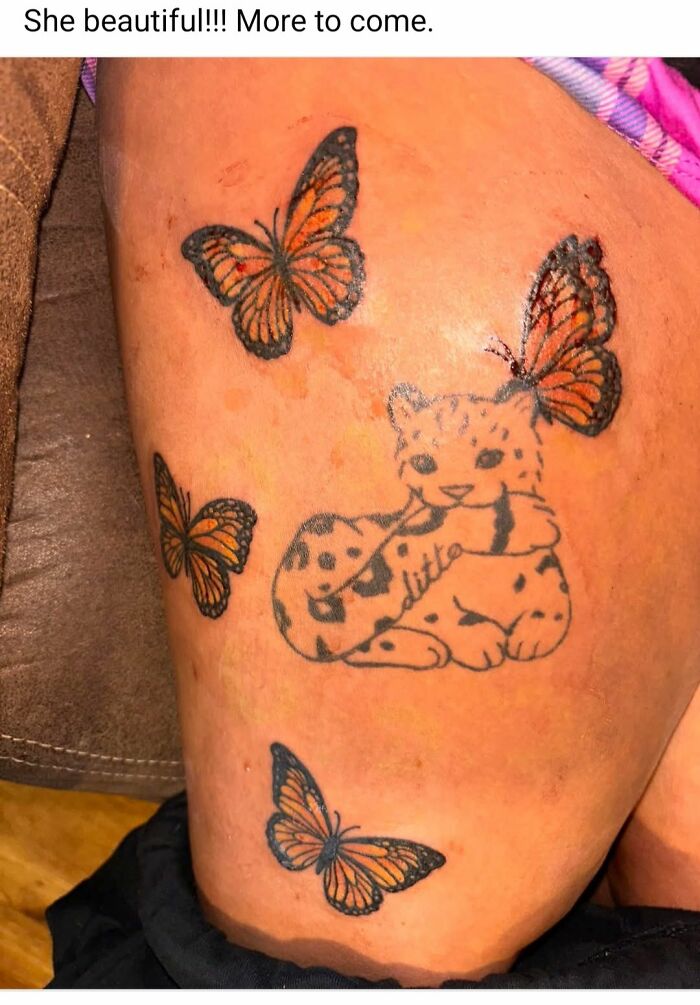 Tattoo of a spotted cat surrounded by orange and black butterflies on a person's leg in a worst tattoos online group.