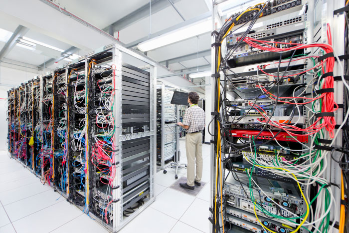 Technician monitoring servers in a data center filled with complex wiring highlighting AI industry infrastructure and secrets.